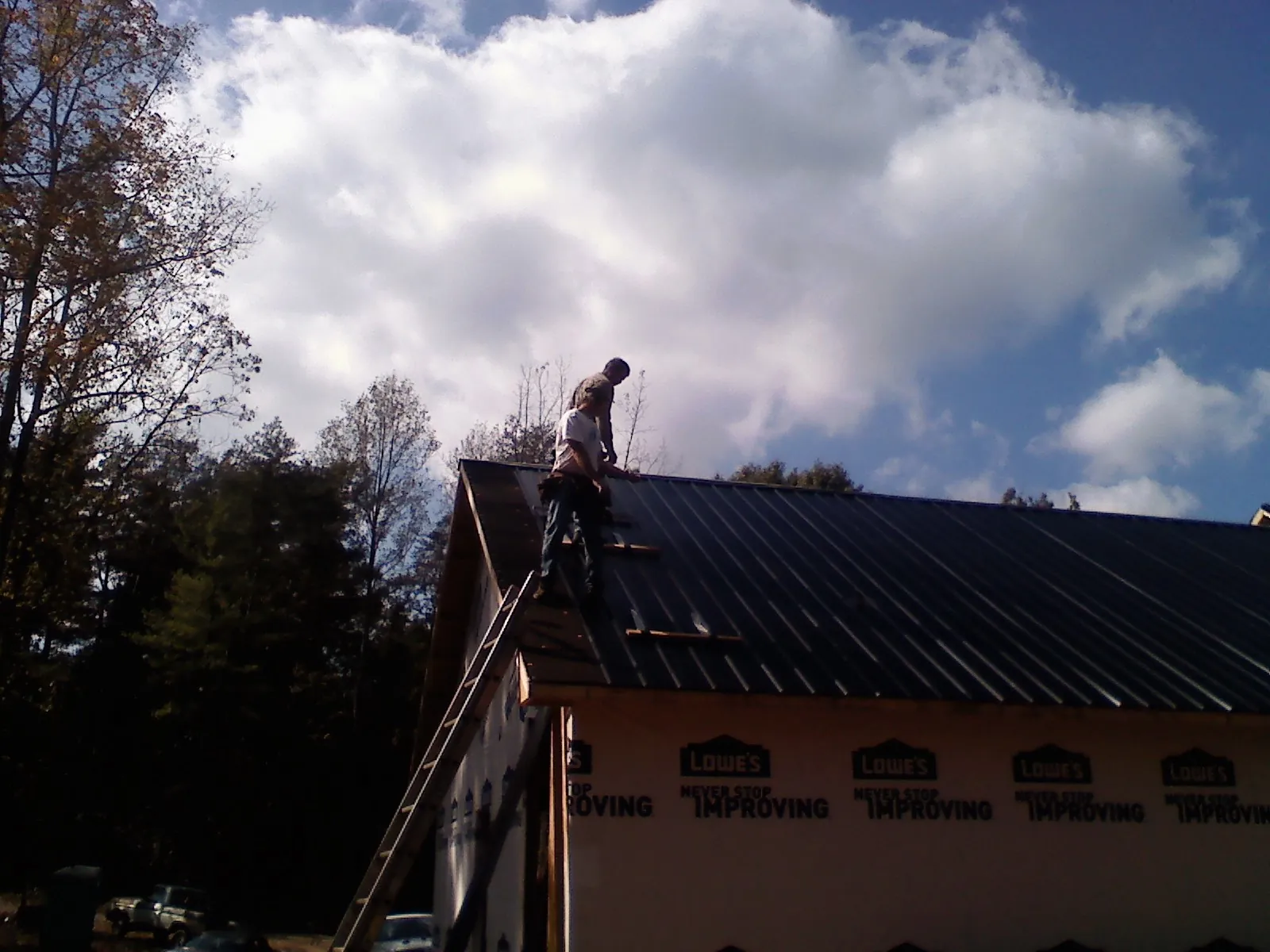 Roofer fastening dark metal panels high against a cloudy sky, from a Roof Inspection job in Stratford